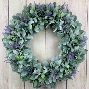 May include: A green and purple wreath made of faux greenery and lavender. The wreath is made of a variety of different types of leaves and flowers.