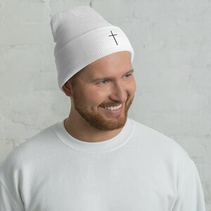 May include: White beanie with a black cross embroidered on the front.