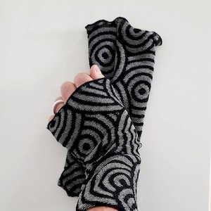 Könnte beinhalten: Fingerlose Handschuhe mit schwarzem und silbernem Muster und einem Rüschenrand.