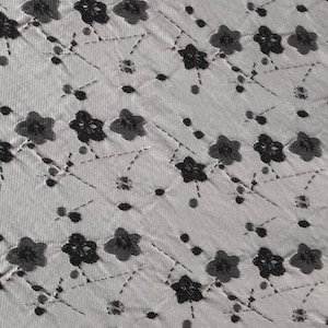 Könnte beinhalten: Weißer Stoff mit einem schwarzen Blumenmuster. Die Blumen sind klein und haben ein fünfblättriges Design. Der Stoff hat eine subtile Textur.