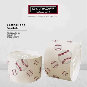 May include: Two cylindrical lampshades with a baseball theme. The lampshades are off-white with a pattern of baseballs in red and white. The text "DYANKOFF DECOR" and "LAMPSHADE /baseball/" is visible.
