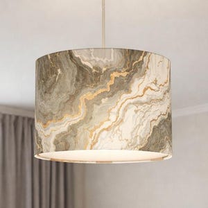 Może przedstawiać: Cylindryczna lampa wisząca z kloszem w kształcie bębna, ozdobiona marmurkowym wzorem w odcieniach szałwiowej zieleni, kremu i bieli, podkreślona cienkimi, płynnymi żyłkami w kolorze metalicznego złota na całej zewnętrznej powierzchni.