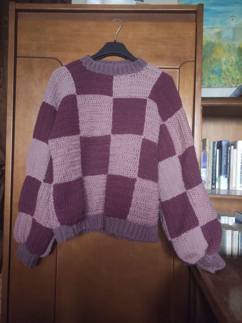 K&ouml;nnte beinhalten: Ein geh&auml;kelter Pullover mit einem karierten Muster in Lila- und Rosat&ouml;nen.