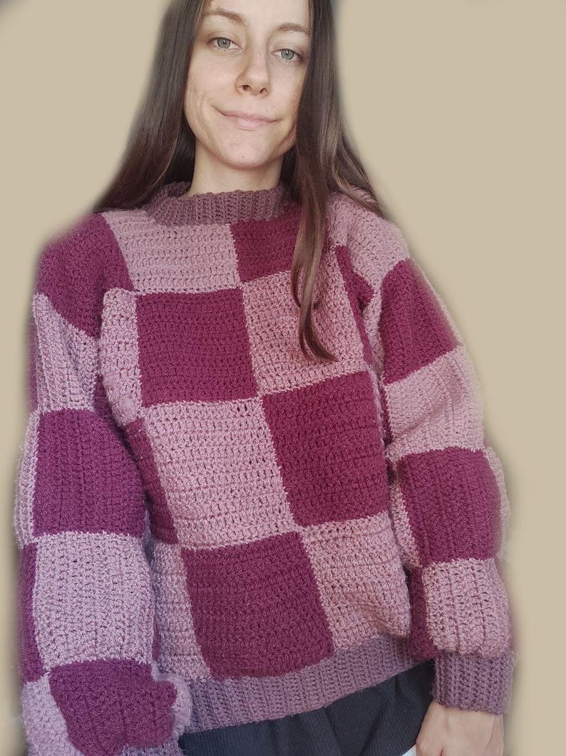 K&ouml;nnte beinhalten: Ein geh&auml;kelter Pullover mit einem karierten Muster in Rosa- und Lilat&ouml;nen.
