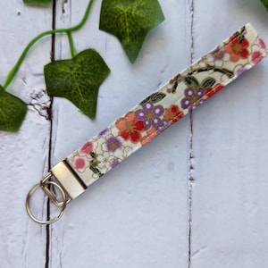 May include: A white fabric key chain with a floral pattern in shades of pink, red, and purple. The key chain has a silver metal ring.