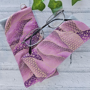May include: Purple and gold patterned fabric eyeglasses case with a pair of black framed glasses inside.