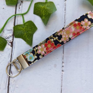 May include: A black fabric keychain with a floral pattern in pink, red, and gold. The keychain has a silver metal ring.