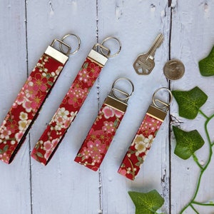 May include: Five red and gold floral patterned keychains with silver key rings. The keychains are all different lengths.