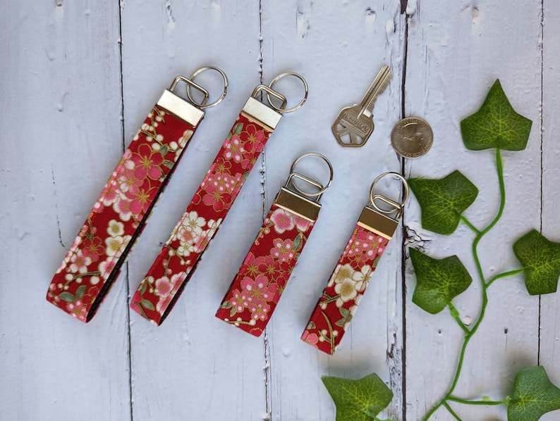 May include: Five red and gold floral patterned keychains with silver key rings. The keychains are all different lengths.