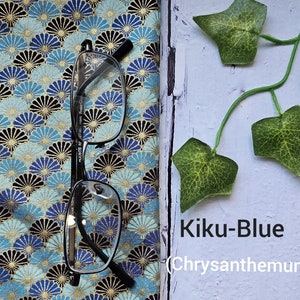 May include: A pair of eyeglasses on a blue and gold fabric with a chrysanthemum pattern. The fabric has the text "Kiku-Blue (Chrysanthemum)" printed on it.