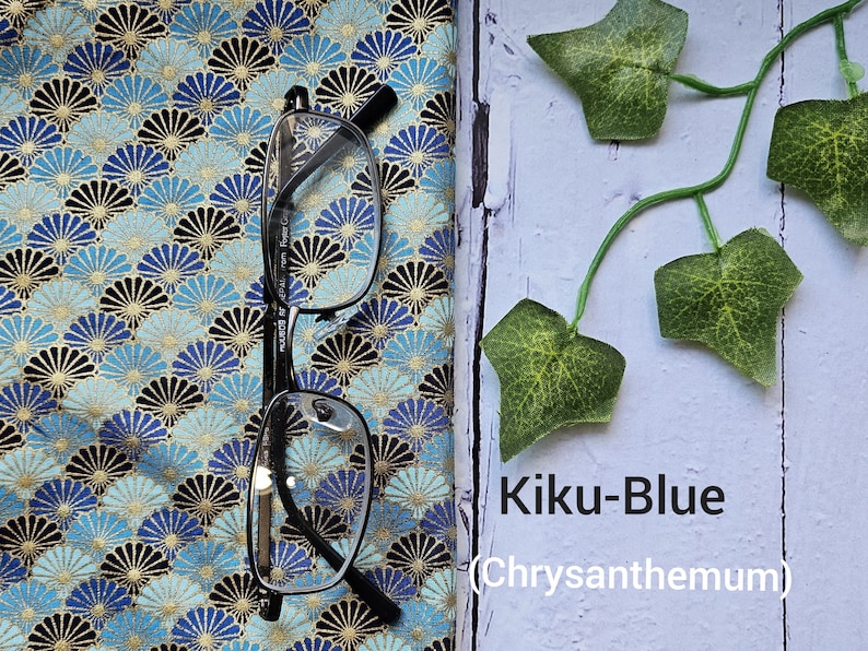 May include: A pair of eyeglasses on a blue and gold fabric with a chrysanthemum pattern. The fabric has the text "Kiku-Blue (Chrysanthemum)" printed on it.