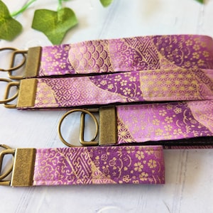 May include: Four purple and gold fabric keychains with brass key rings. The fabric has a traditional Japanese pattern.