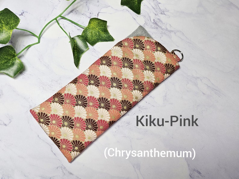 May include: A pink and brown fabric eyeglass case with a chrysanthemum pattern. The case has a silver zipper pull and the text "Kiku-Pink (Chrysanthemum)" is printed on the white background.