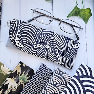 May include: Eyeglass case with a navy blue and white wave pattern, next to a pair of eyeglasses. Several fabric samples with Japanese-inspired designs are also visible, including geometric and floral patterns.