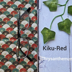 May include: A pair of eyeglasses on a fabric with a red, white, and green pattern. The fabric has a repeating design of stylized chrysanthemums. The text "Kiku-Red (Chrysanthemum)" is written on a light blue surface.
