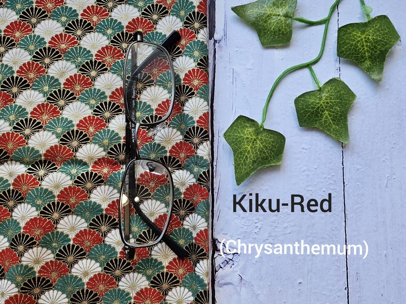 May include: A pair of eyeglasses on a fabric with a red, white, and green pattern. The fabric has a repeating design of stylized chrysanthemums. The text "Kiku-Red (Chrysanthemum)" is written on a light blue surface.