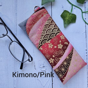 May include: A pink and gold fabric eyeglass case with a Japanese-inspired pattern. The case has a zipper closure and a small loop for attaching a keychain. The text "Kimono/Pink" is printed on the case.