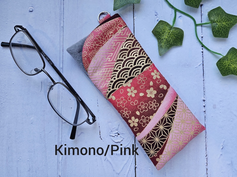 May include: A pink and gold fabric eyeglass case with a Japanese-inspired pattern. The case has a zipper closure and a small loop for attaching a keychain. The text "Kimono/Pink" is printed on the case.