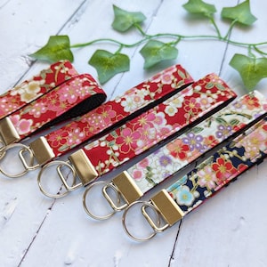 May include: Five keychains with silver key rings and fabric straps featuring a floral pattern in shades of red, pink, white, and gold. The fabric is a Japanese-inspired design with cherry blossoms.