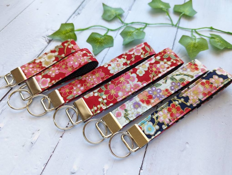 May include: Five keychains with silver key rings and fabric straps featuring a floral pattern in shades of red, pink, white, and gold. The fabric is a Japanese-inspired design with cherry blossoms.