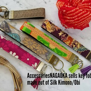 May include: Five colorful key fobs made from silk kimono and obi fabric. Each fob has a silver key ring and a tassel. The text on the image reads "AccessoriesNAGAOAKA sells key fobs made out of Silk Kimono/Obi".