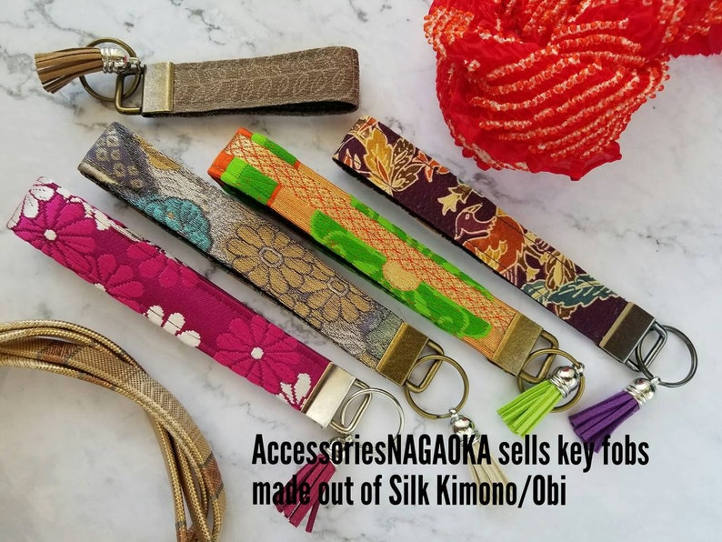 May include: Five colorful key fobs made from silk kimono and obi fabric. Each fob has a silver key ring and a tassel. The text on the image reads "AccessoriesNAGAOAKA sells key fobs made out of Silk Kimono/Obi".