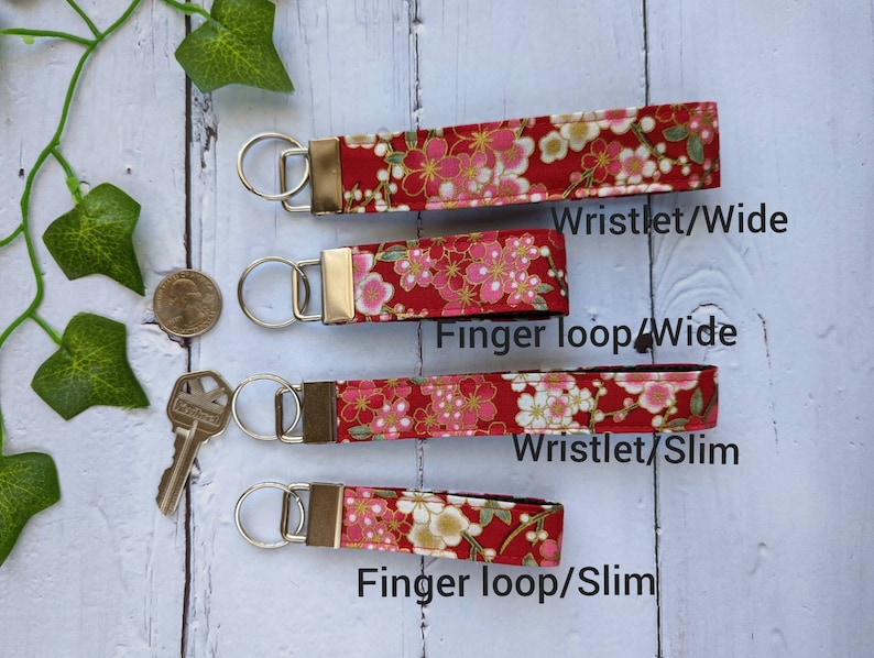 May include: Four red fabric keychains with a floral pattern. The keychains are available in two styles: wristlet and finger loop, and two widths: wide and slim. The text "Wristlet/Wide", "Finger loop/Wide", "Wristlet/Slim", and "Finger loop/Slim" is printed below each keychain.