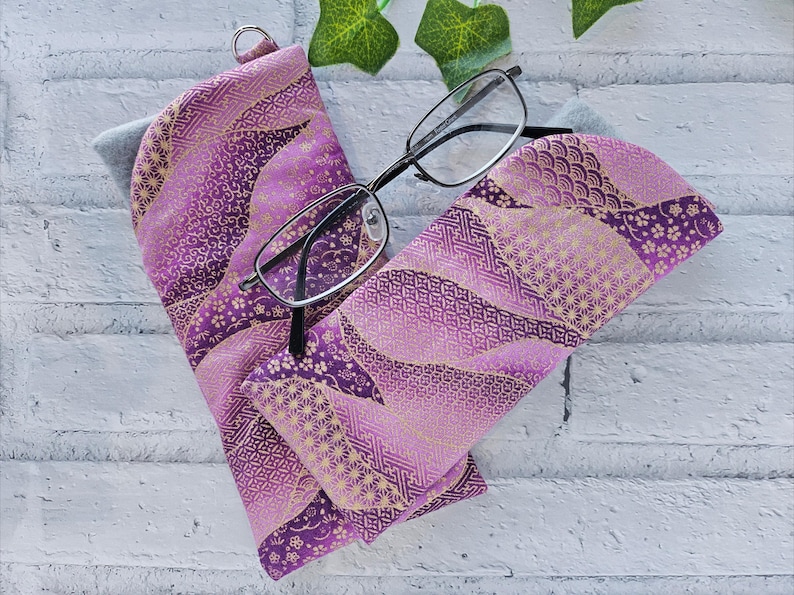 May include: Purple and gold patterned fabric eyeglasses case with a pair of black framed glasses inside.