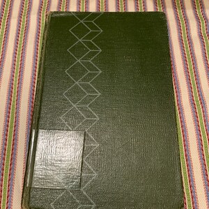 以下が含まれることがあります： 表紙に幾何学模様が施された濃い緑色のハードカバーの本。背表紙には白いラベルが付いています。