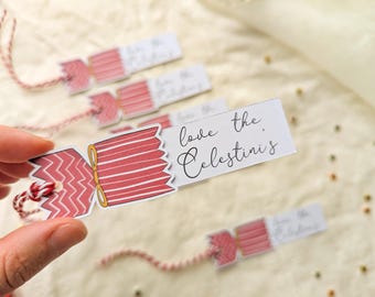 May include: A rectangular paper gift tag featuring a red and white chevron patterned cracker graphic with a yellow tie. The white tag displays the black cursive text "love the Celestini's" and includes a red and white twisted twine string.
