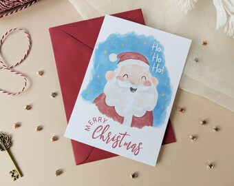 May include: A white greeting card featuring a watercolor illustration of Santa Claus with a red hat and white beard against a blue background with yellow stars. The text reads Ho Ho Ho! and Merry Christmas in red script. A dark red envelope is underneath.