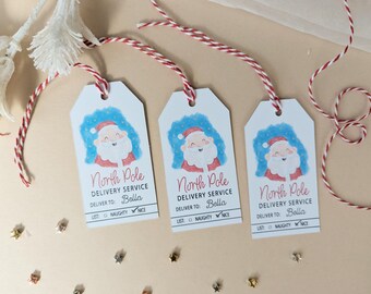 May include: Three white rectangular gift tags with red and white baker's twine. Each tag features a watercolor illustration of Santa Claus, the text North Pole DELIVERY SERVICE, DELIVER TO: Bella, and a checkbox list for NAUGHTY or NICE.