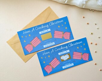 May include: Two rectangular blue scratch-off cards with the text Have A Cracking Christmas, To Holly, and From Joseph. The cards feature pink and white striped Christmas cracker illustrations, gold stars, and a gold scratch-off panel.