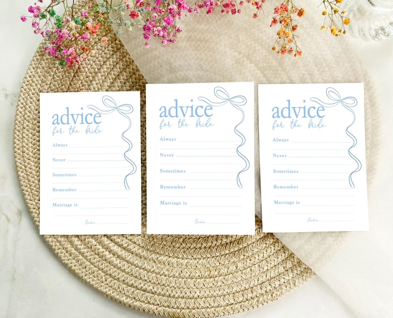 以下が含まれることがあります： 青いリボン模様の白いカードが3枚あり、それぞれに「花嫁へのアドバイス」という文字が印刷されています。各カードには、ゲストが花嫁へのアドバイスを書くためのプロンプトがリストされており、「常に」、「決して」、「時々」、「覚えておいて」、「結婚とは」などが含まれています。