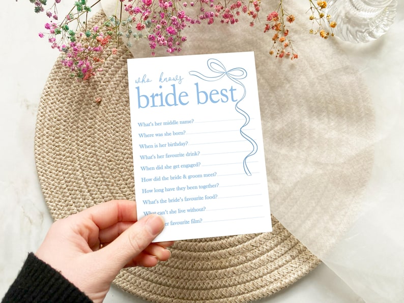 以下が含まれることがあります： 青いと白い印刷可能なブライダルシャワーゲームカード。テキストは「花嫁を一番よく知っているのは誰？」。花嫁に関する質問のリストがあります。