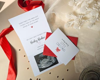 May include: A white pregnancy announcement card featuring a black and white ultrasound image, the text "SOMETIMES THE SMALLEST THINGS TAKE UP THE MOST ROOM IN YOUR HEART", "WE CAN'T WAIT TO MEET YOU BABY BAKER", and a smaller white card with "a very merry LITTLE CHRISTMAS".