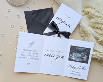 May include: A white tri-fold pregnancy announcement card with black text reading A LITTLE surprise, SOMETIMES THE SMALLEST THINGS TAKE UP THE MOST ROOM IN YOUR HEART, WE CAN'T WAIT TO meet you, Baby Baker, and ARRIVING MARCH 2027, featuring a sonogram image.