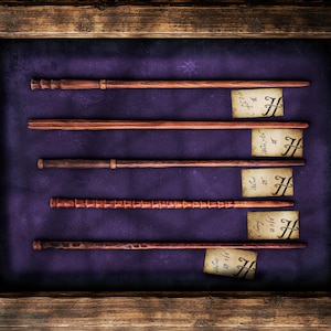 Peut inclure: Présentation encadrée en bois avec cinq baguettes marron de différents modèles, sur fond de velours violet. Chaque baguette est accompagnée d'une petite étiquette en papier vieilli avec la lettre "H". Le cadre a des coins métalliques.