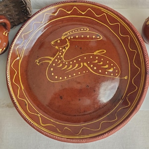May include: A terracotta plate with a hand-painted rabbit design in yellow. The plate has a wavy yellow border and a textured rim. The plate is part of a set, with other terracotta pieces visible in the image.