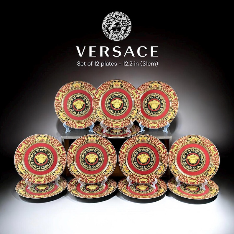 Op de afbeelding: Een set van 12 decoratieve borden, elk met een diameter van 31 cm. De borden hebben een rood en goudkleurig ontwerp met een centraal zwart medaillon en een gouden embleem. De borden zijn op een donkere ondergrond geplaatst.