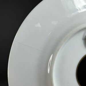 Puede incluir: Primer plano de un plato de cer&aacute;mica blanca con borde dorado y centro negro. El plato tiene un acabado brillante y se puede ver una ligera grieta. El plato est&aacute; sobre un fondo oscuro.