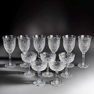 May include: A set of clear crystal glassware, comprising stemmed wine glasses and coupe glasses. The glasses have an intricate, cut-glass design and are set on decorative bases. The arrangement implies a formal setting or special event.