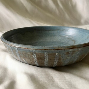 May include: A light blue ceramic bowl with a white and brown patterned design. The bowl is slightly speckled and has a rounded shape.