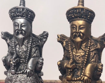 May include: Two chess pieces, one silver and one gold, depicting a seated figure with a crown and ornate clothing. The pieces are on a red and black chequered chessboard.