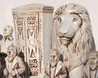 May include: A white ceramic chess set featuring a lion, a castle, and several figures. The figures are all dressed in clothing and have beards. The chess pieces are on a black and white chequered board.
