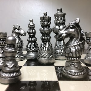 May include: A set of silver chess pieces on a black and white chequered board. The pieces include a knight, a rook, a pawn, a bishop, and a queen.