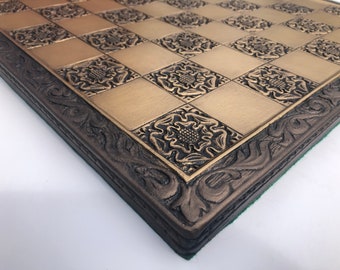 May include: A close-up of a brown and gold chessboard with an ornate border. The board is made of wood and has a green felt lining.