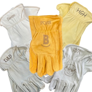 May include: Five leather work gloves with different names embroidered on them. The gloves are in various shades of tan and white. The names are Sean, Dad, Pops, Riva, and HGH.