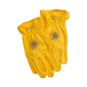 May include: A pair of yellow leather work gloves with a sunflower design and the initials "MNS" embroidered on each glove.