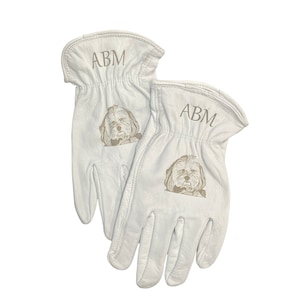 May include: A pair of white leather work gloves with a dog's face and the initials "ABM" embroidered on each glove.